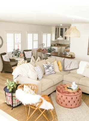 Un salon comprenant un canapé d’angle, un pouf rond, un fauteuil en osier et une petite table d’appoint sur laquelle est posée une plante.