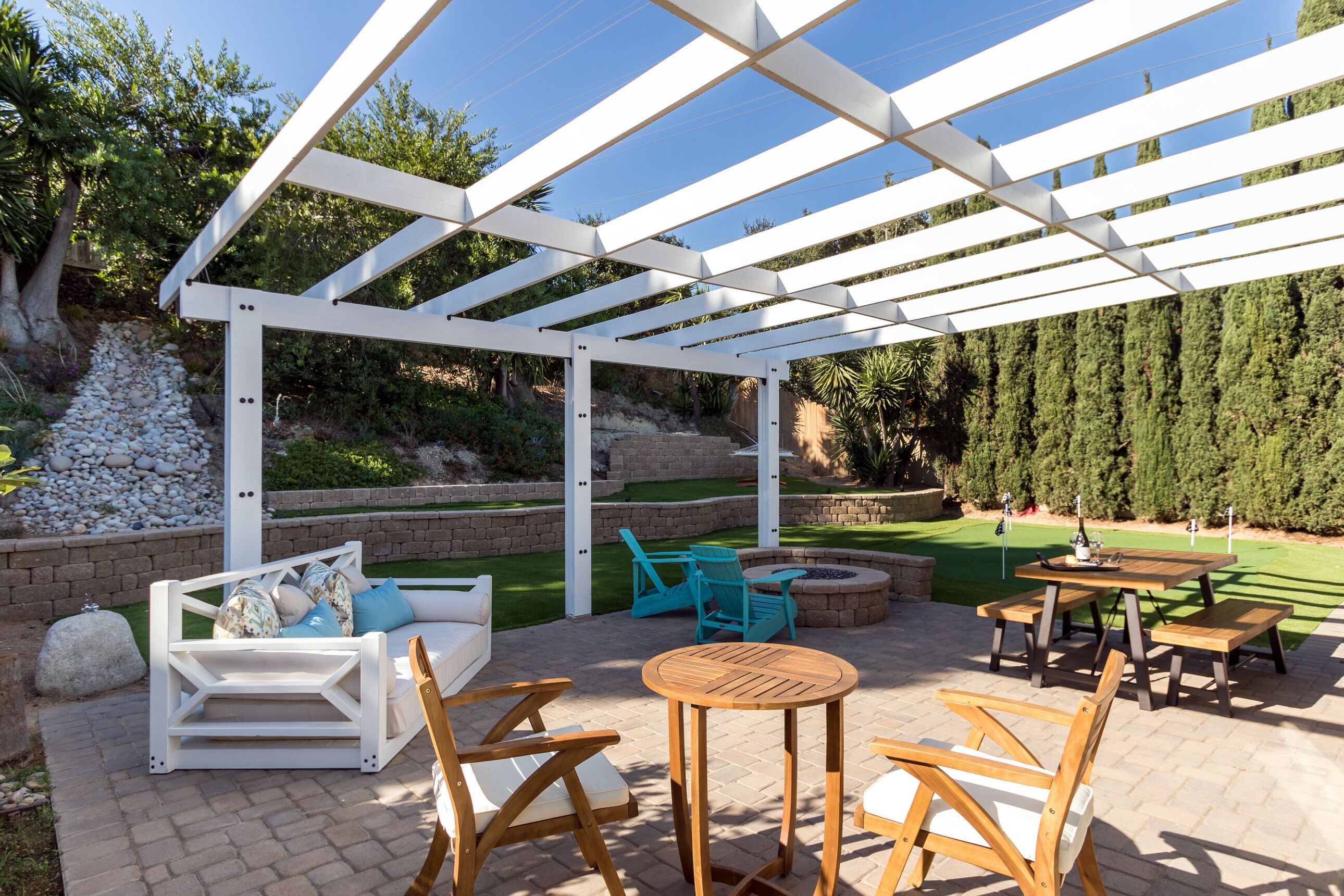 A covered patio area with outdoor furniture, a wooden table, and a white pergola structure.