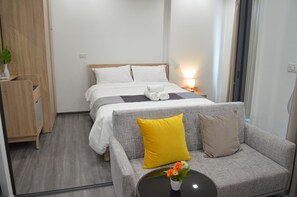 A hotel room with a bed, a sofa, a small table with a vase of flowers, and a nightstand with a lamp.