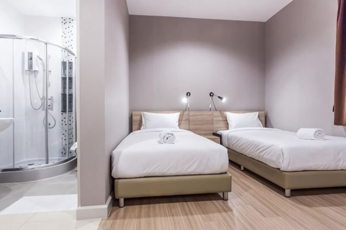 A hotel room with a shower, two beds, and a bedside table with lamps.