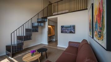 Una sala de estar moderna con una escalera, un sofá, una mesa de centro y un televisor montado en la pared.