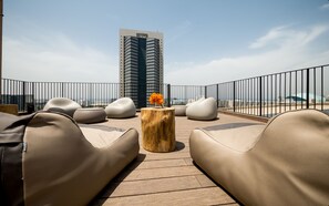 A rooftop lounge with modern seating and a wooden table, overlooking a cityscape. - La Cappella Hotel (Haifa)