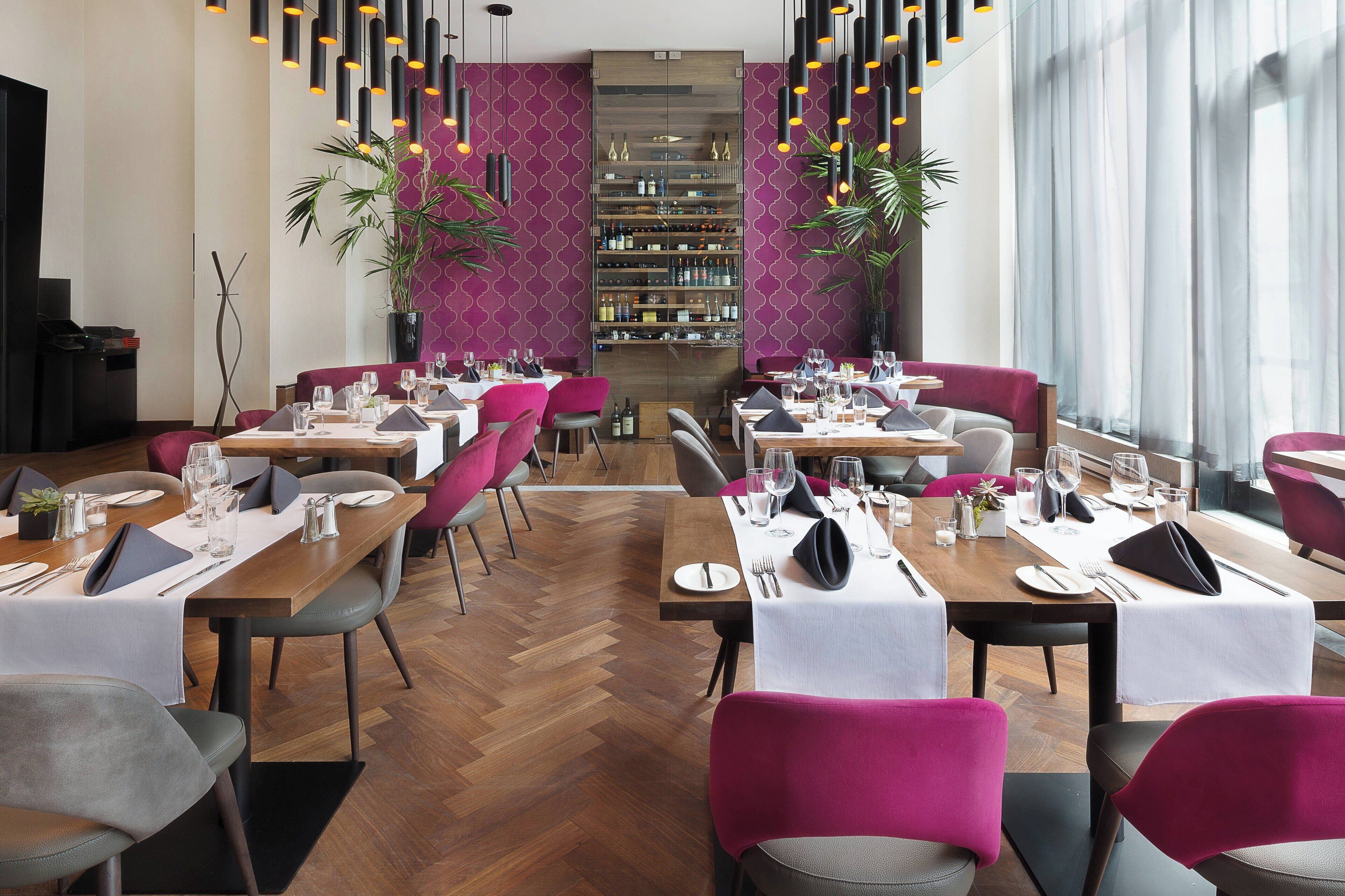 A restaurant with wooden tables, purple chairs, and a wine rack in the background.