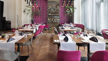 A restaurant with wooden tables, purple chairs, and a wine rack in the background.