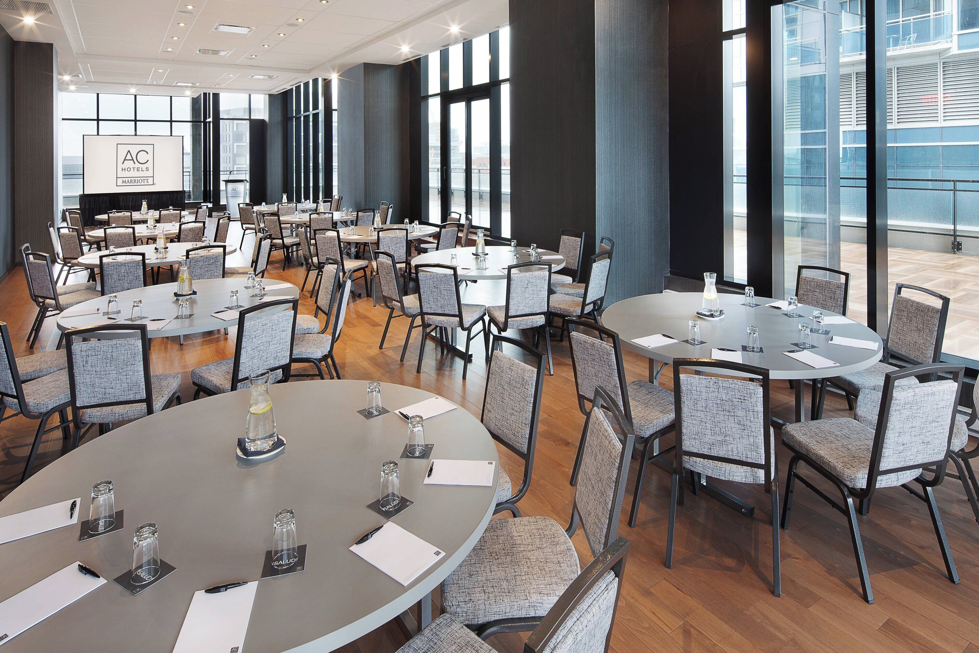 Une grande salle de conférence dotée de nombreuses tables rondes, chacune étant équipée de chaises, de porte-noms et de verres.