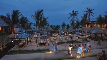A resort with outdoor dining areas, palm trees, and a beach view.