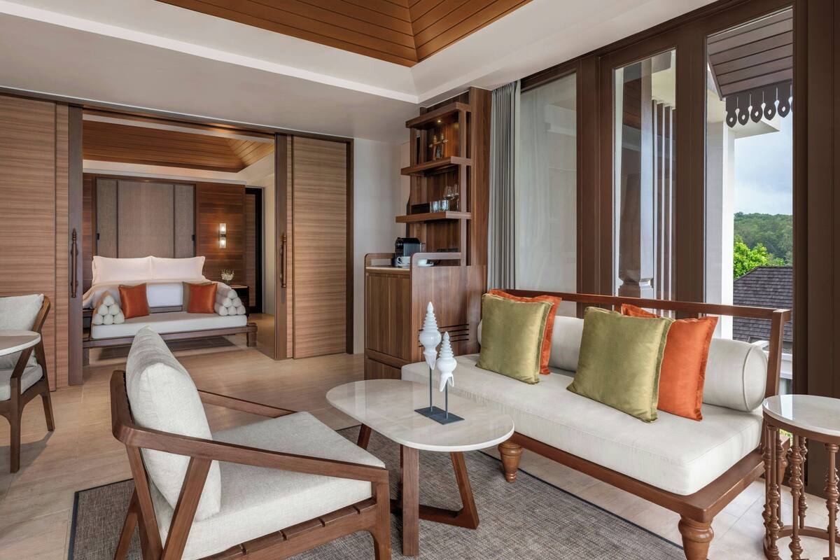 Una habitación de hotel moderna con sofá, sillas, una mesa de centro y una estantería.