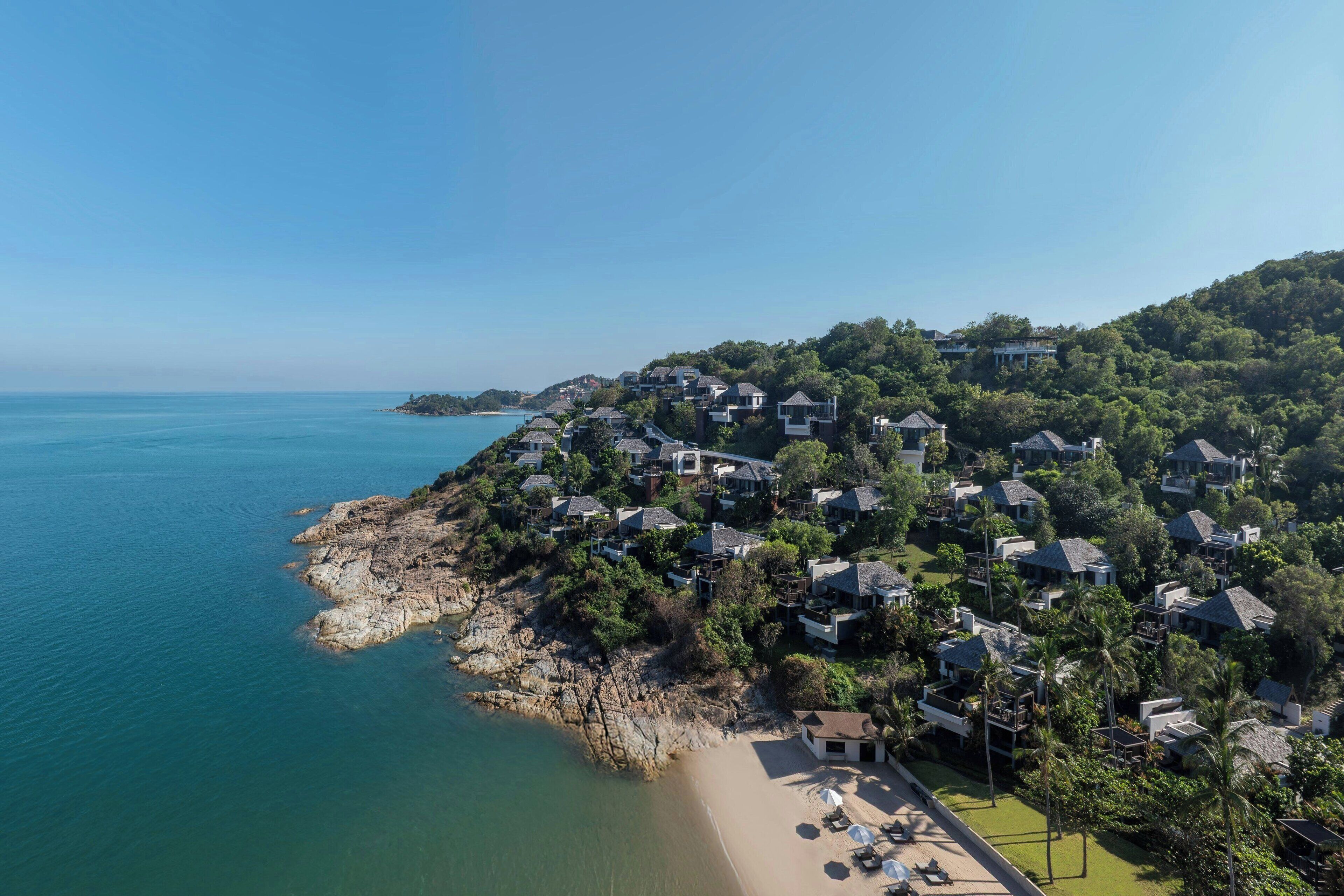 An aerial view of a coastal residential area with houses, a beach, and a clear blue sky.