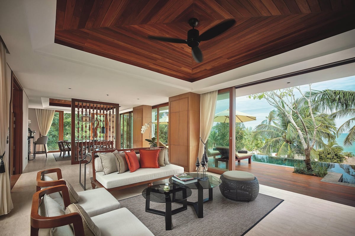 Amplia sala de estar con techo de madera, ventanas grandes, un conjunto de sofás y vista al océano.