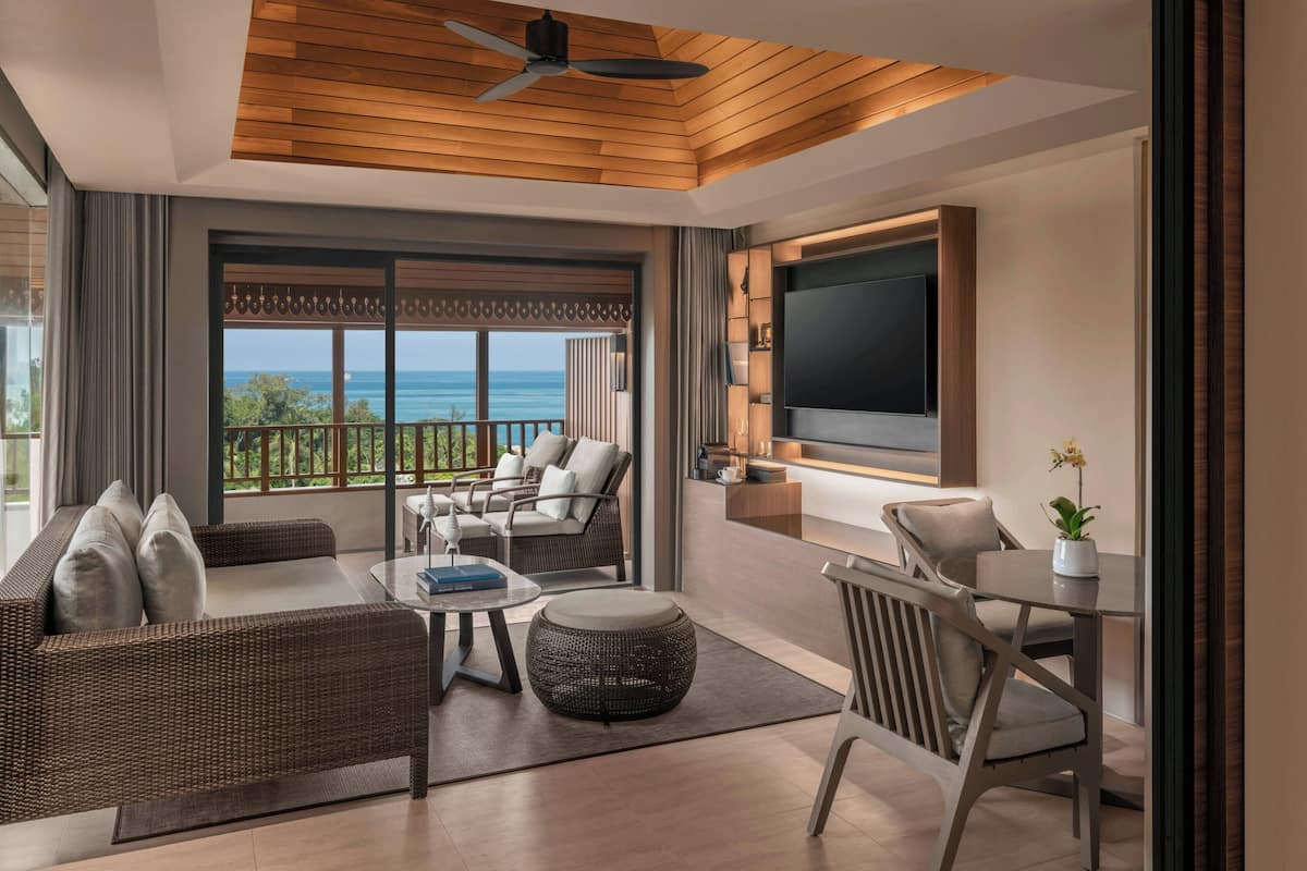 Una sala de estar moderna con un televisor grande, asientos cómodos, un balcón con vista al mar y un ventilador de techo.