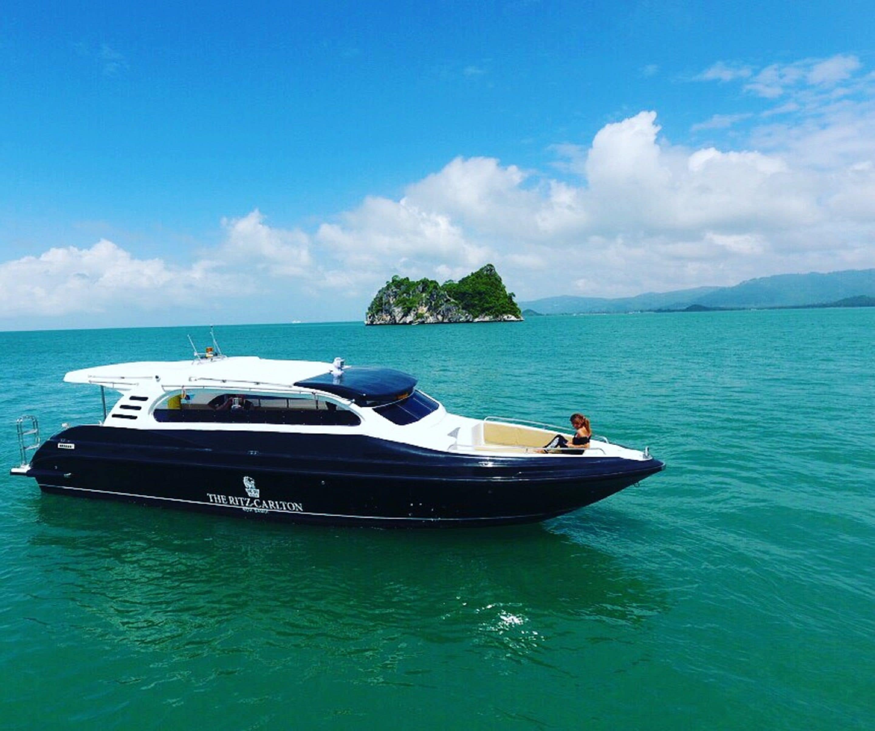 Un yate llamado "The Ritz-Carlton" en aguas turquesas tranquilas, con una pequeña isla al fondo.