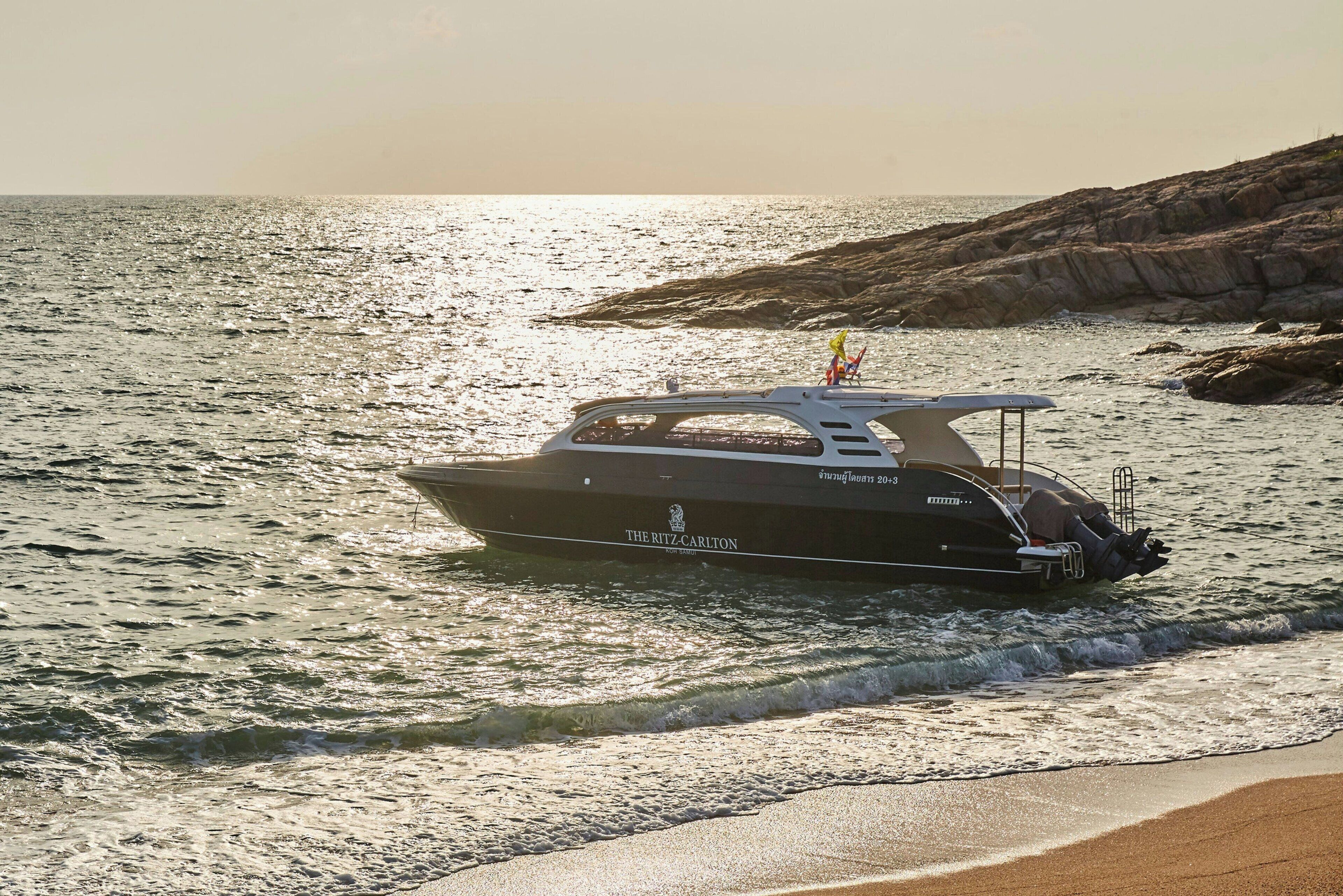 Un bateau nommé « The Ritz Carlton » navigue sur une étendue d’eau près d’une côte rocheuse.
