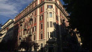 Un immeuble à plusieurs étages, de style architectural classique, avec une entrée d’angle, de grandes fenêtres et un balcon aux étages supérieurs.
