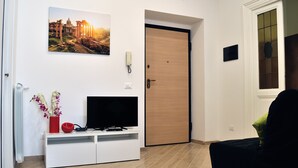 Une pièce comprenant un meuble de rangement blanc pour appareils multimédias, un téléviseur, une porte avec un panneau en verre et un tableau encadré accroché au mur.