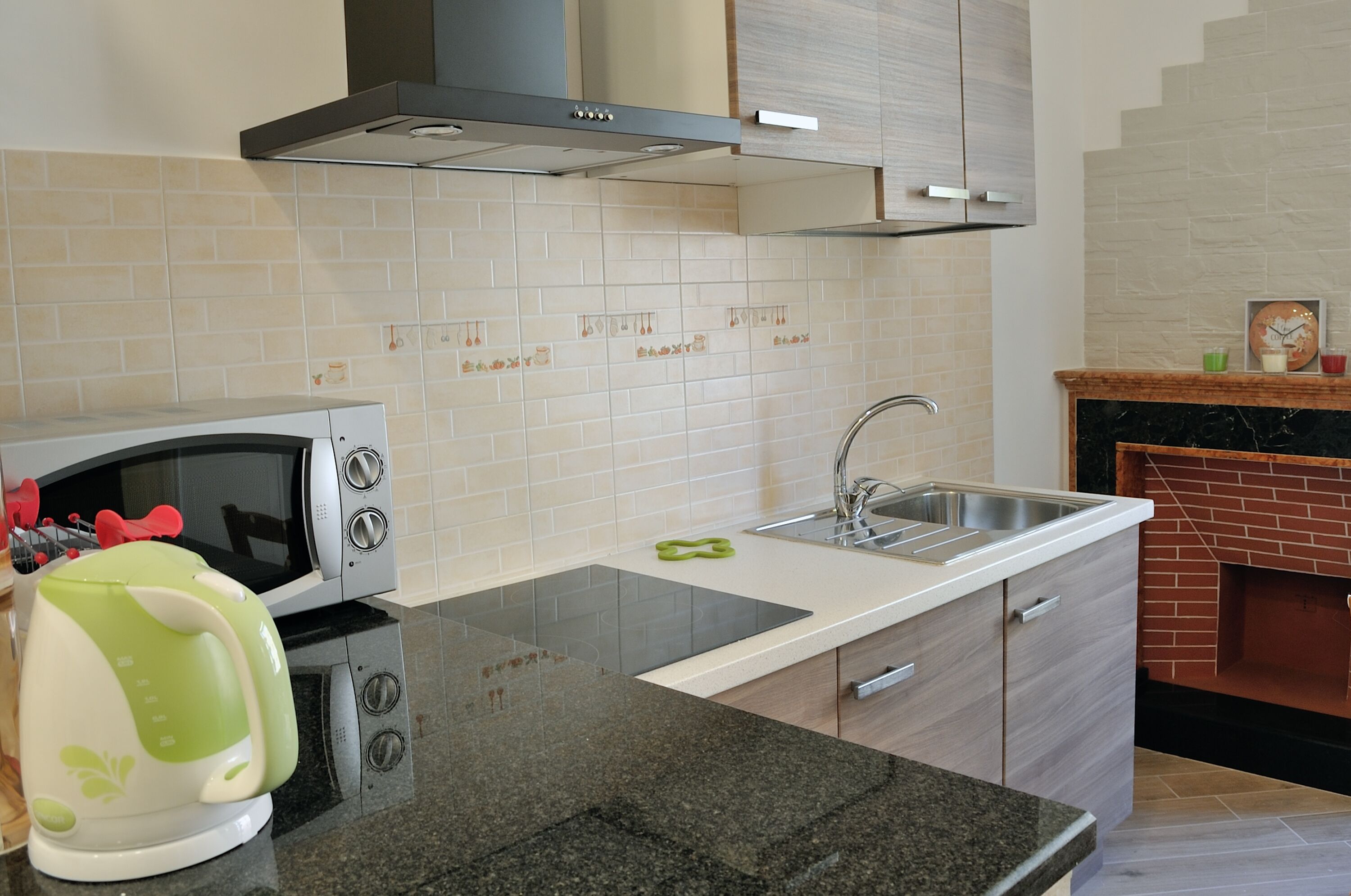 A modern kitchen with a microwave, kettle, sink, and a brick fireplace.