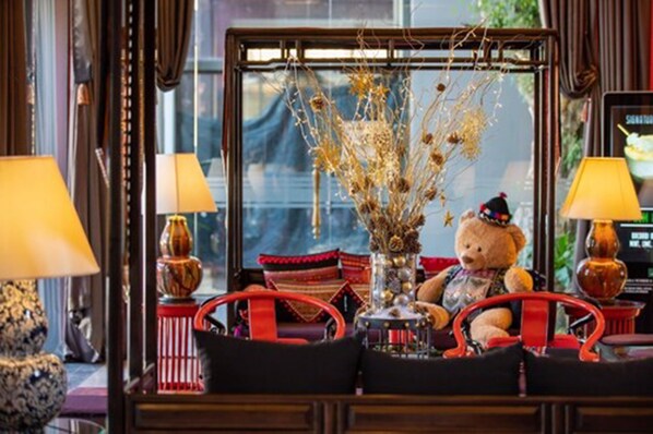 A cozy seating area with a teddy bear, a vase with dried branches, and two lamps.