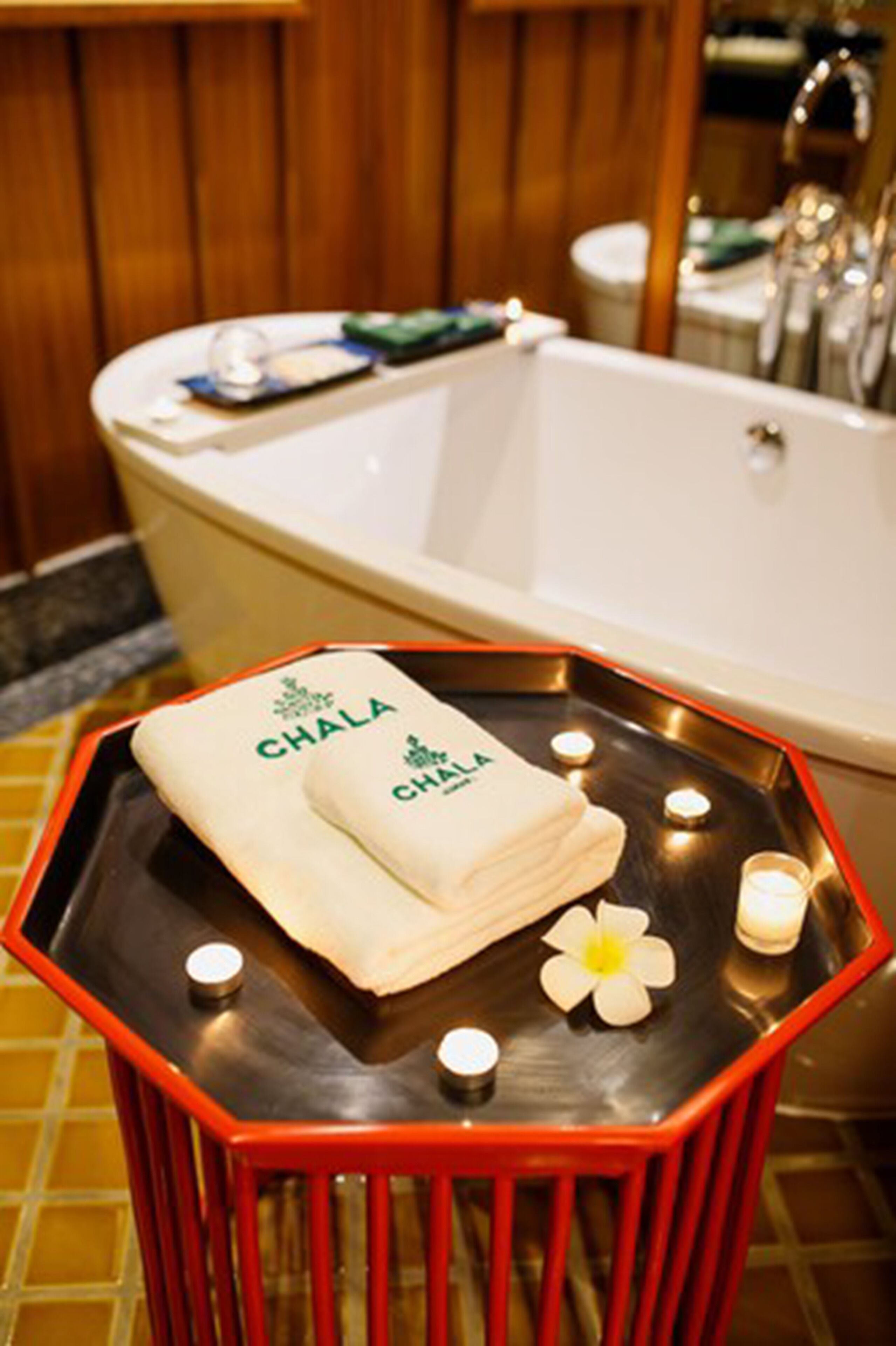 Un baño con una bañera, un taburete rojo con una toalla y velas.