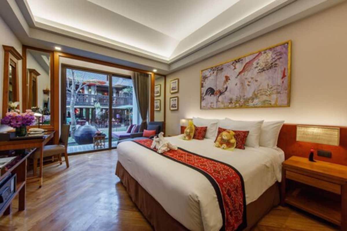 A spacious bedroom with a large bed, a desk with a chair, and a view of a traditional building through a glass door.