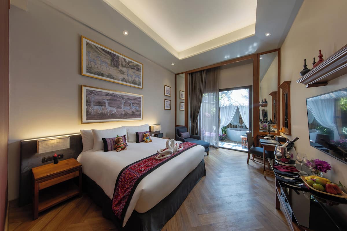 A spacious hotel room with a large bed, a desk with a computer, a dining area, and a balcony with a view.