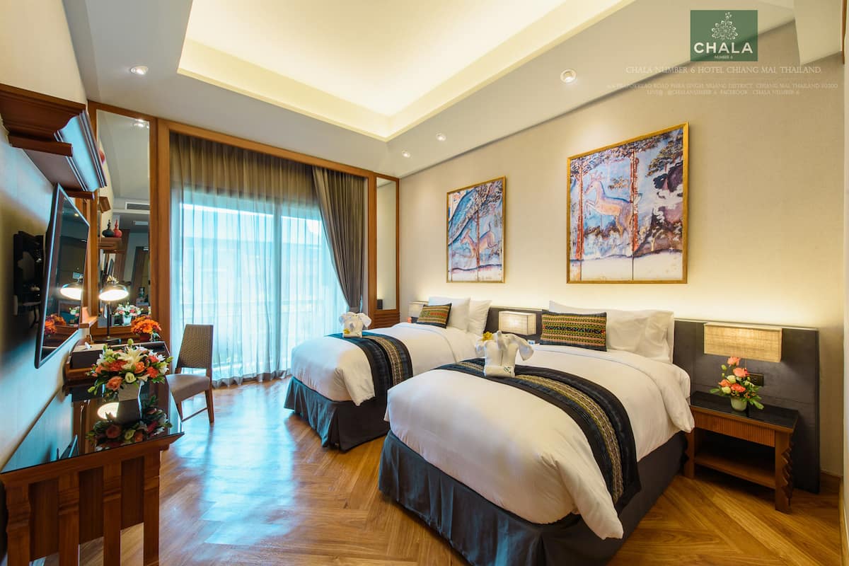A hotel room with two beds, a desk with a chair, a TV, and artwork on the walls.