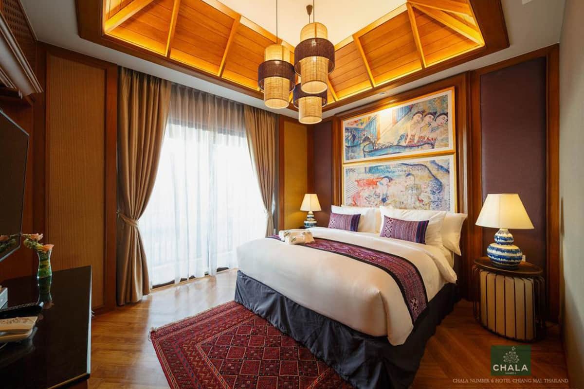 A hotel room with a large bed, two bedside tables with lamps, a painting on the wall, and a view of the outside through the window.