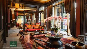A spacious lobby with a red sofa, a traditional tea set, and a large window with curtains. - Chala Number 6 Hotel (Chiang Mai)