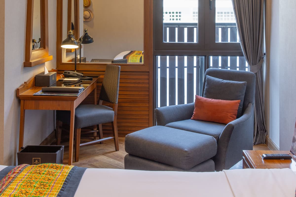 A hotel room with a bed, a desk with a lamp, a chair, and a balcony with a view.