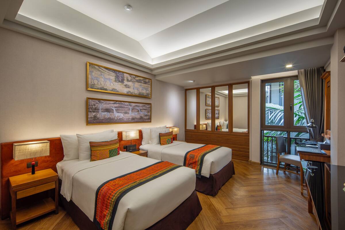 A hotel room with two beds, wooden floors, a balcony with a view, and artwork on the walls.