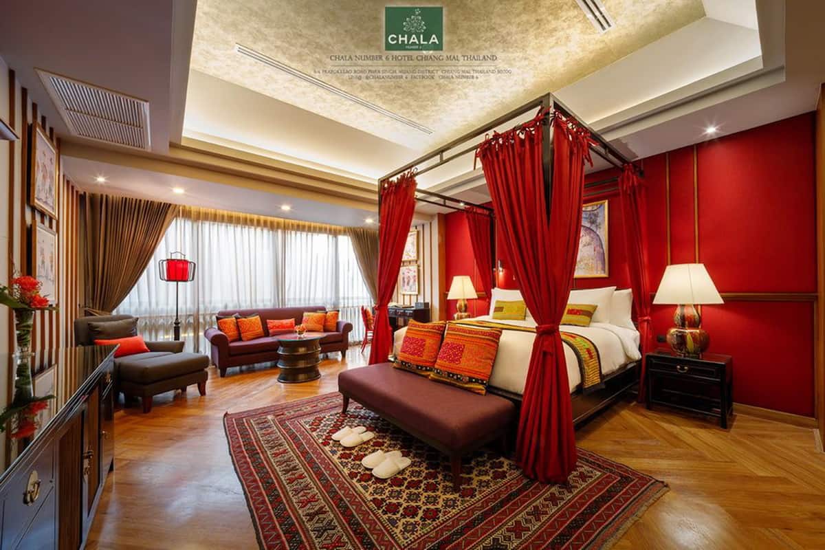 A spacious hotel room with a large bed, a sitting area with a sofa and armchairs, a dining table, and a red curtain.