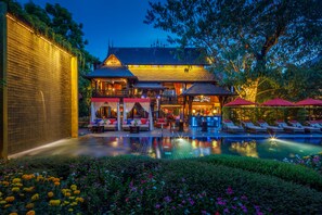 A traditional building with a swimming pool, outdoor seating, and a well-lit bar area.