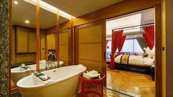 Un baño de hotel con una bañera grande, zona de ducha separada y un dormitorio con cama, cortinas y ventana.