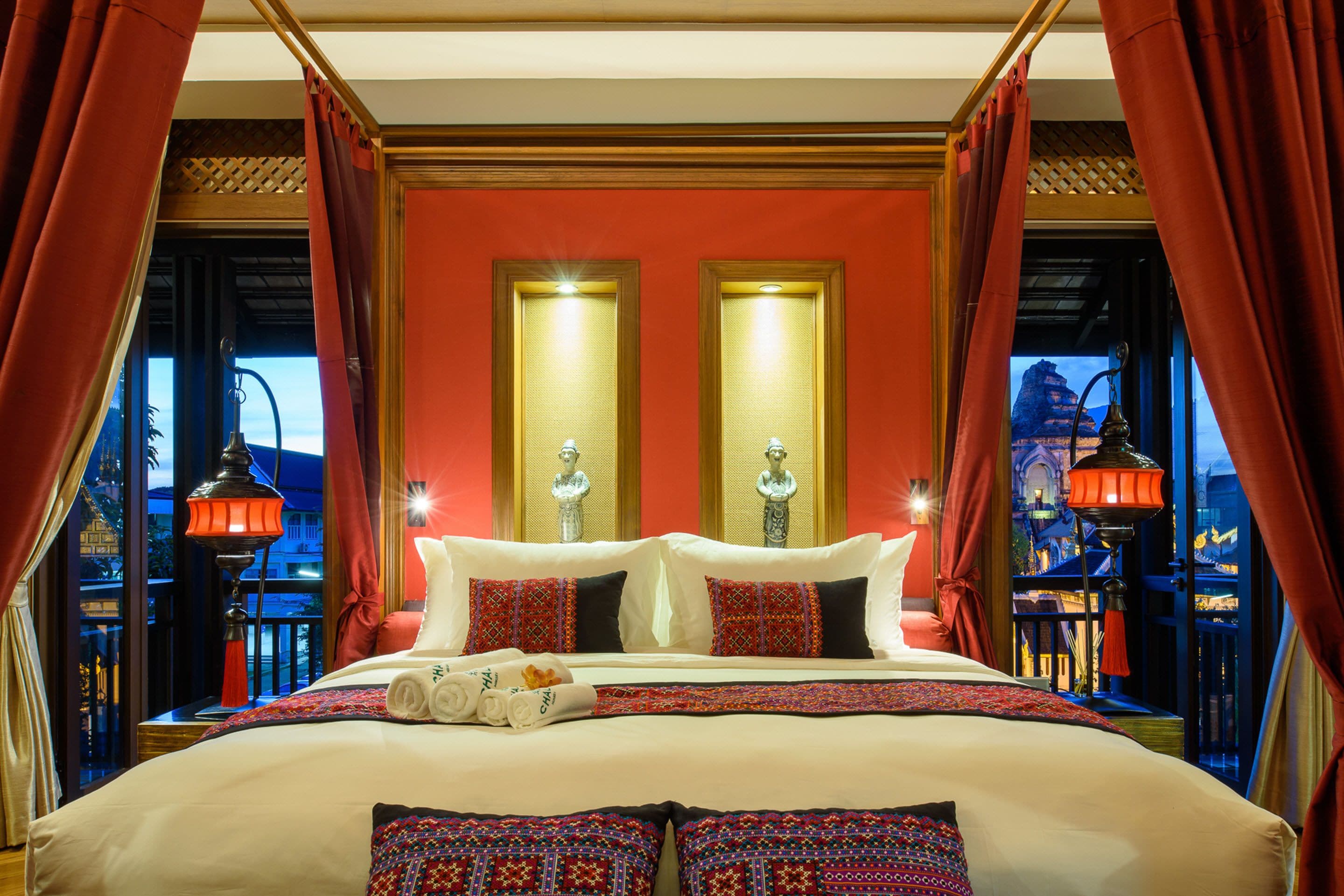 Una cama grande con cortinas rojas, dos apliques en la pared y vistas de una montaña a través de la ventana.
