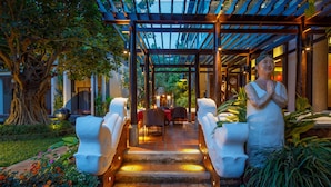 A covered outdoor area with a table and chairs, a statue, and a tree. - Chala Number 6 Hotel (Chiang Mai)