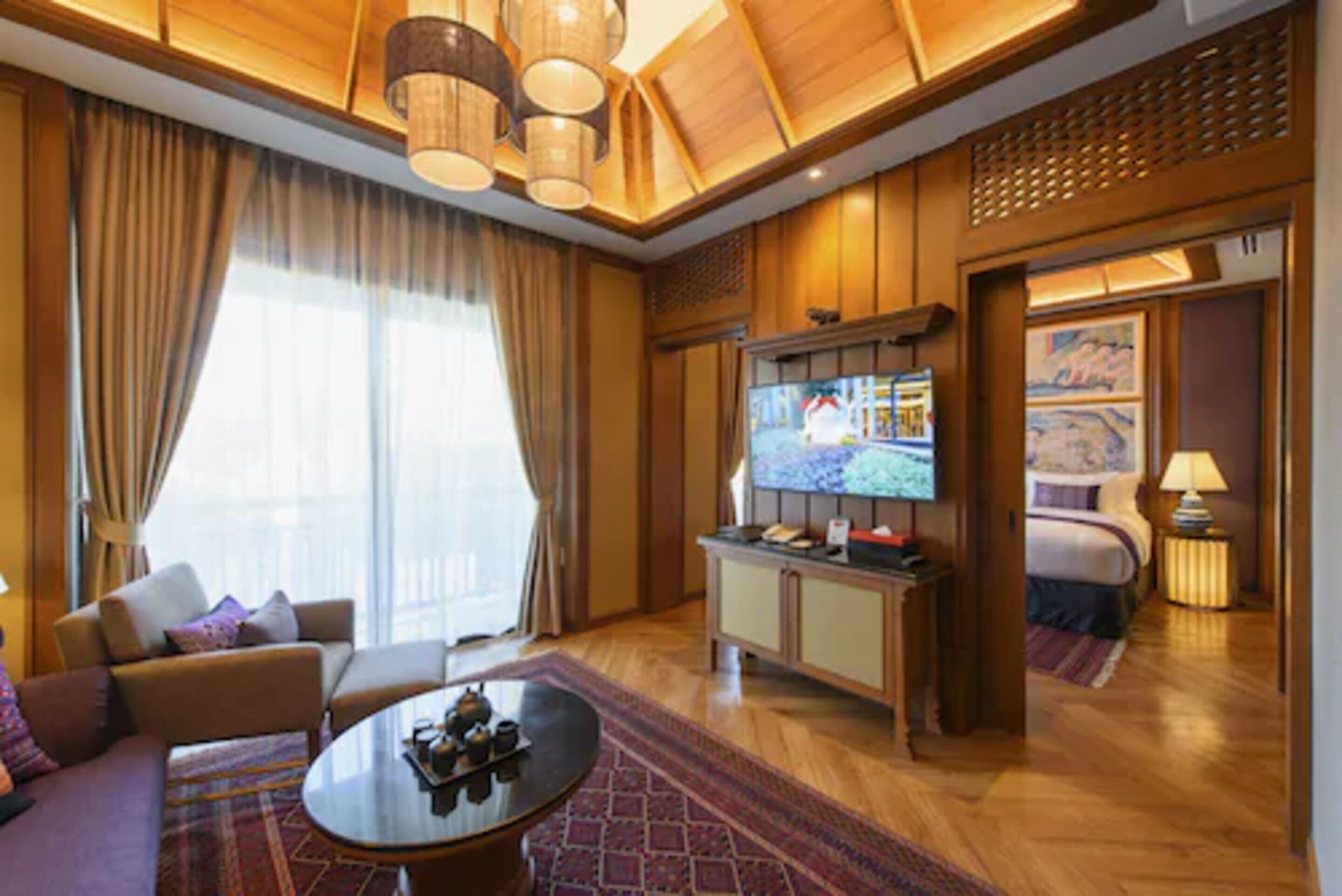 A hotel room with a wooden ceiling, a television, a bed, a sofa, and a dining table.