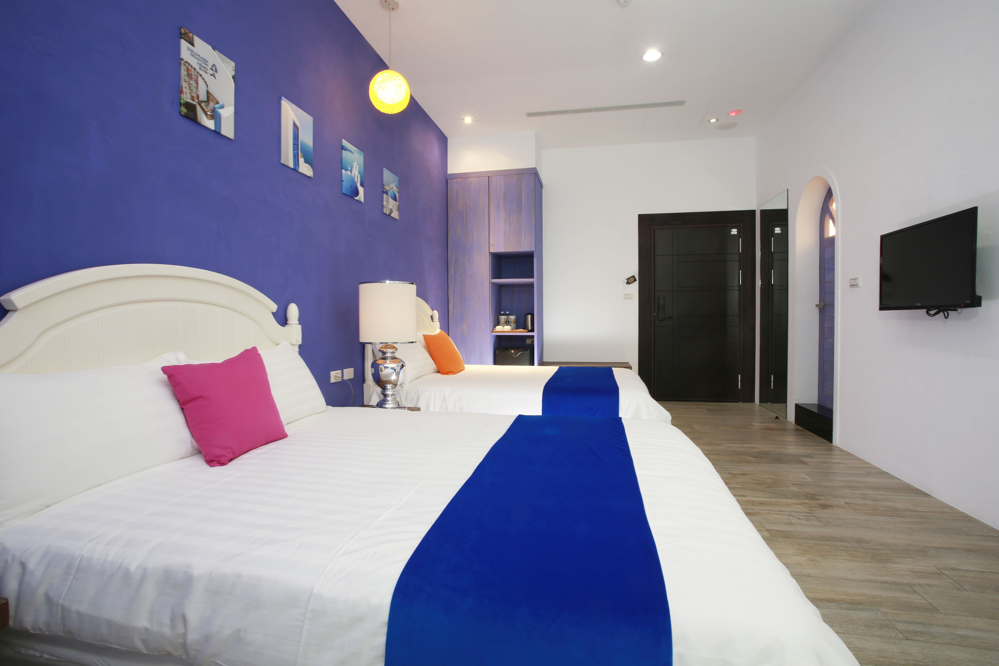 A hotel room with two beds, a TV, a lamp, and a blue runner.