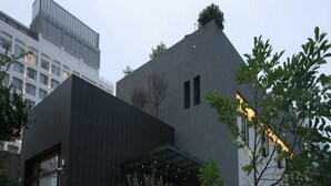 A modern building with a dark facade, a glass entrance, and a small tree in the foreground. - Green Life Spa (Jiaoxi)