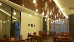 A restaurant with multiple wooden tables and chairs, pendant lighting, and a stone accent wall. - Green Life Spa (Jiaoxi)