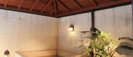 Un área de spa con un jacuzzi de piedra, una mesita con un farol y plantas en macetas.