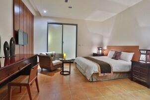 Habitación de hotel con cama, escritorio, silla, televisor y puerta corrediza.