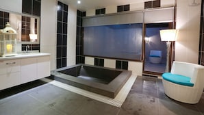 A modern bathroom with a large bathtub, a white wicker chair, and a mirror with a decorative frame. - Green Life Spa (Jiaoxi)