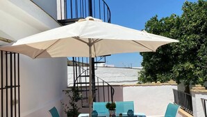 Un patio con un paraguas blanco, sillas color turquesa y una escalera de caracol.