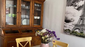 Un comedor con una mesa de madera, sillas, un aparador con puertas de cristal y un cuadro de la Torre Eiffel.