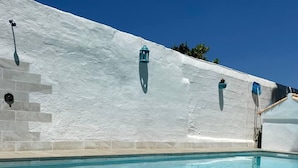Una piscina con un muro blanco y escalones revestidos de azulejos para acceder a ella.