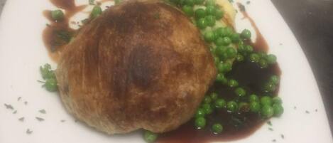A square plate with a round, browned item, possibly a pastry, and green peas with a brown sauce.