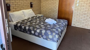 A single bed with a patterned bedspread, a wooden door, and a brick wall. - Shark Bay Hotel (Denham)