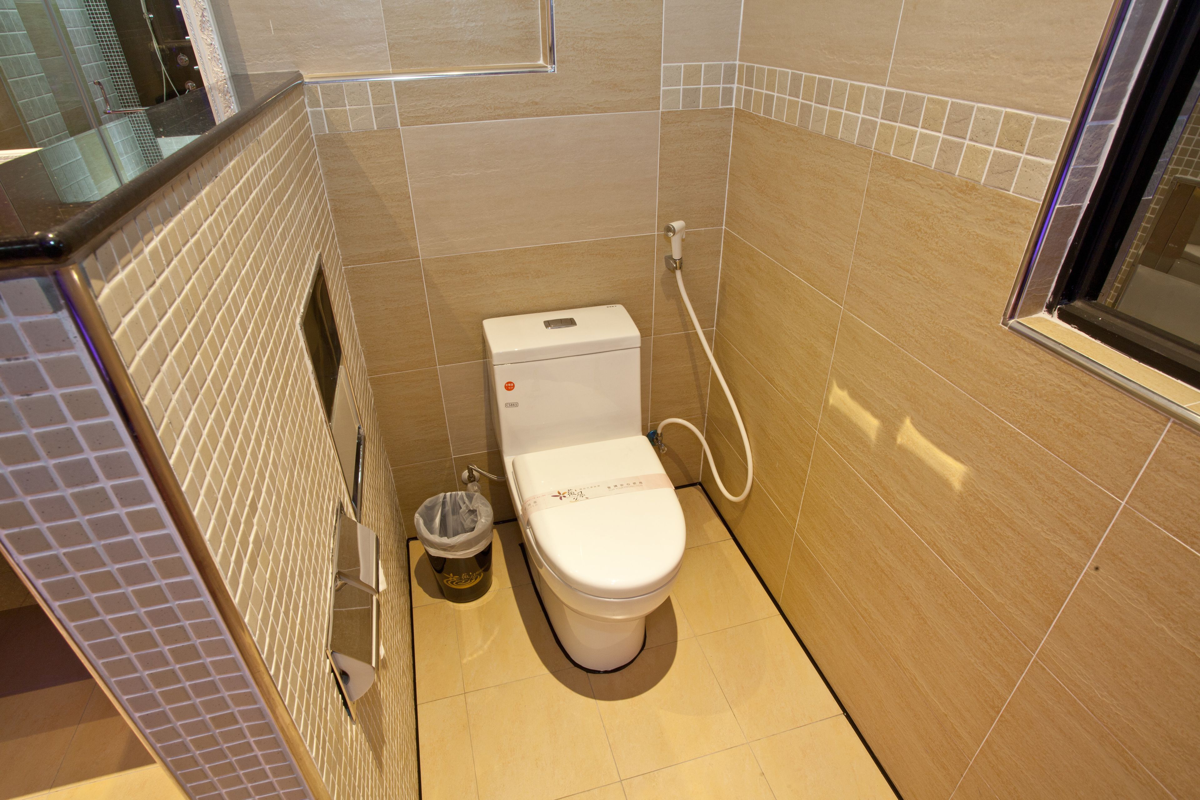 A small, modern bathroom with a toilet, a trash bin, and a shower area.