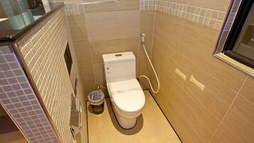 A small, modern bathroom with a toilet, a trash bin, and a shower area.