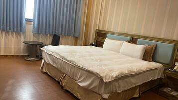 Een hotelkamer met een groot bed, een nachtkastje, een lamp en een raam met gordijnen.