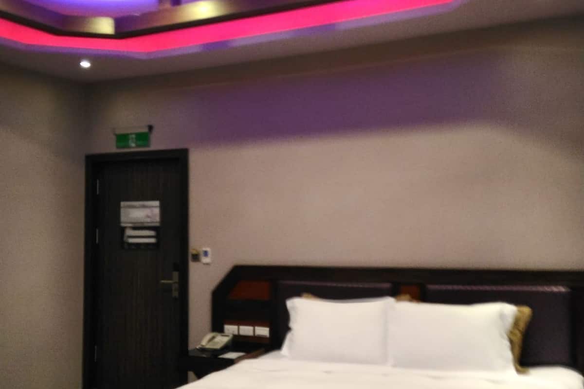 Une chambre d’hôtel avec un lit, une table de chevet, une porte et un plafond doté d’un éclairage encastré.