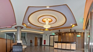 Vestíbulo de hotel de diseño moderno, con una lámpara central, una recepción y una escalera que sube a otro piso.